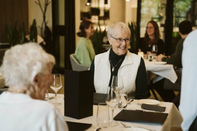 Resident smiling with friends at Summit Dining Room at The Hawthorn, Independent Plus, at Elim Village Garrison Crossing