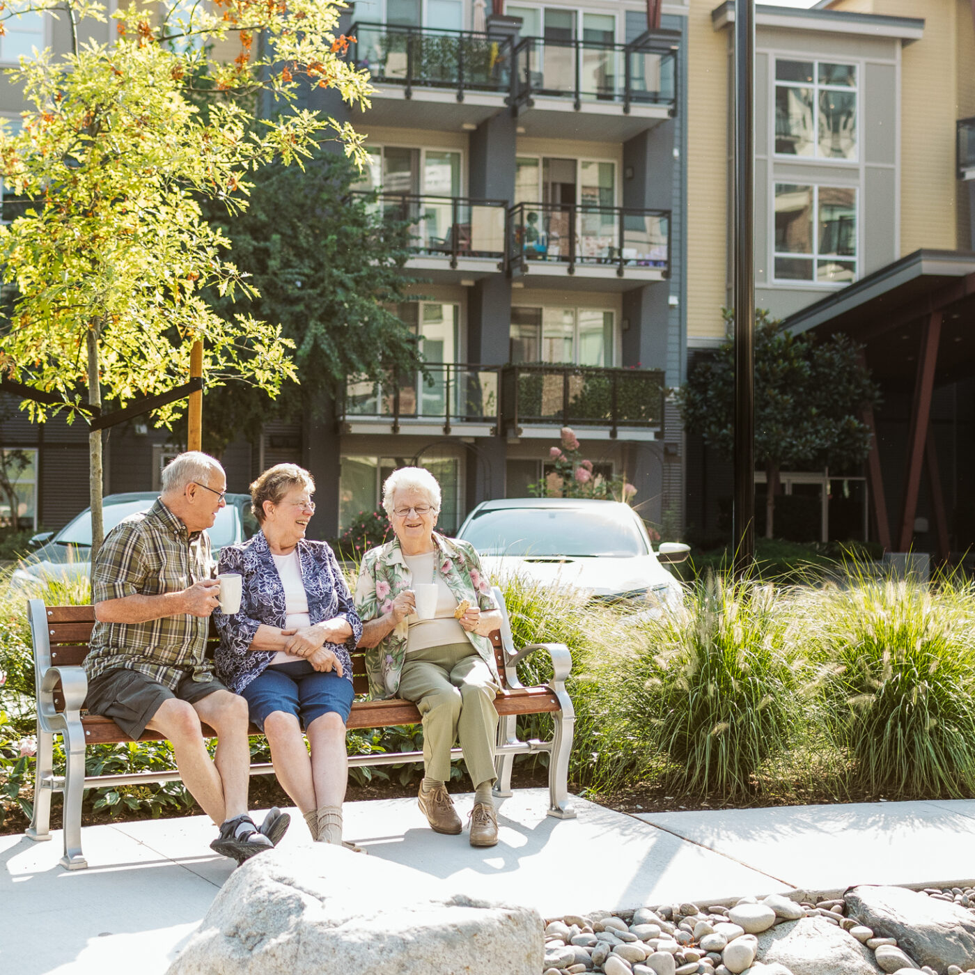 Three ELIM residents sit on a bench outside of The Redwood, ELIM's Senior Rental Apartments in Chilliwack