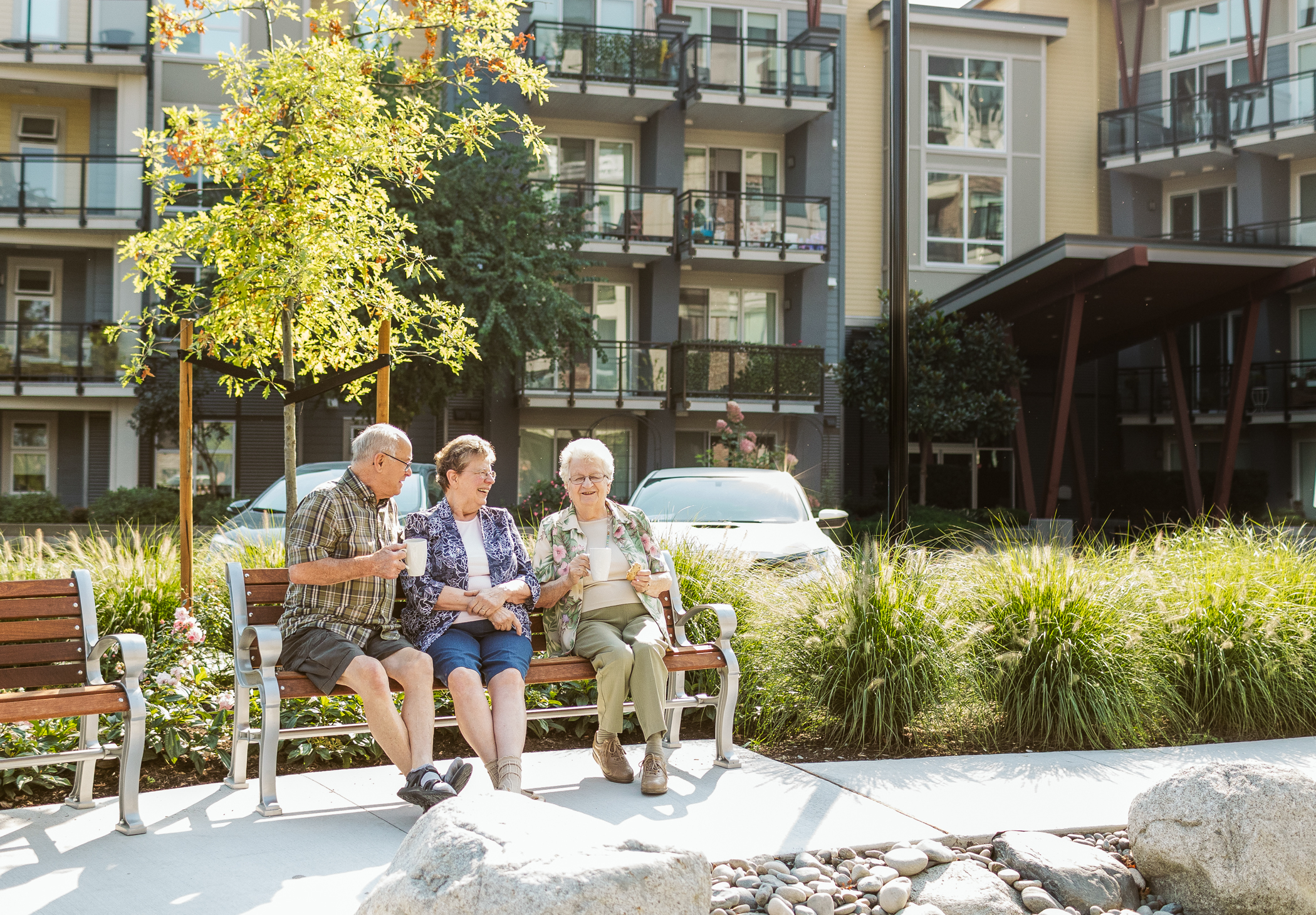 Three ELIM residents sit on a bench outside of The Redwood, ELIM's Senior Rental Apartments in Chilliwack